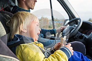 Cute toddler boy, kid sitting on the front seat in child seat on big camper van, smiling