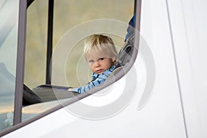 Cute toddler boy, kid sitting on the front seat in child seat on big camper van, smiling