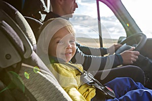 Cute toddler boy, kid sitting on the front seat in child seat on big camper van, smiling