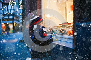 Cute toddler boy looking on car toys in a window on Christmas time season. Fascinated child in winter clothes dreaming