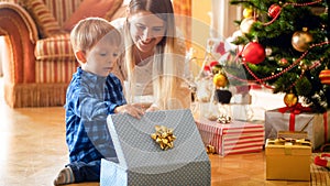 Cute toddler boy looking inside of CHristmas gift box with young mother