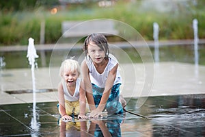 Cute toddler boy and older brothers, playing on a jet fountains with water splashing around