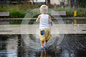 Cute toddler boy and older brothers, playing on a jet fountains with water splashing around