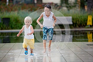 Cute toddler boy and older brothers, playing on a jet fountains with water splashing around