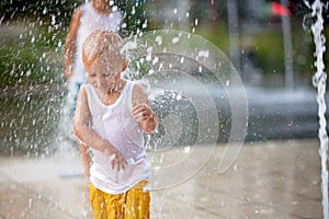 Cute toddler boy and older brothers, playing on a jet fountains with water splashing around