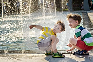 Cute toddler boy and older brothers, playing on a jet fountains with water splashing around, summertime