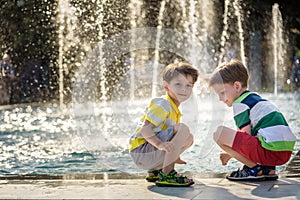 Cute toddler boy and older brothers, playing on a jet fountains with water splashing around, summertime