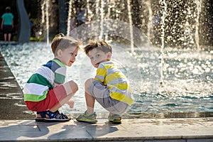 Cute toddler boy and older brothers, playing on a jet fountains with water splashing around, summertime