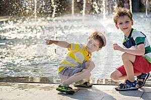 Cute toddler boy and older brothers, playing on a jet fountains with water splashing around, summertime