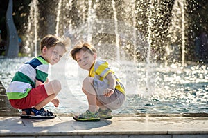 Cute toddler boy and older brothers, playing on a jet fountains with water splashing around, summertime