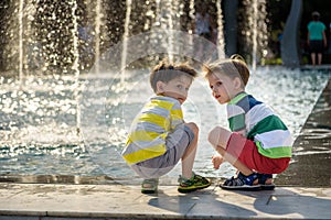 Cute toddler boy and older brothers, playing on a jet fountains with water splashing around, summertime