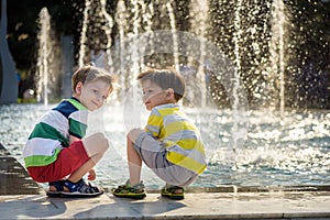 Cute toddler boy and older brothers, playing on a jet fountains with water splashing around, summertime