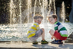 Cute toddler boy and older brothers, playing on a jet fountains with water splashing around, summertime