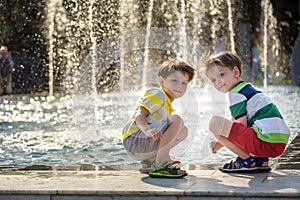 Cute toddler boy and older brothers, playing on a jet fountains with water splashing around, summertime