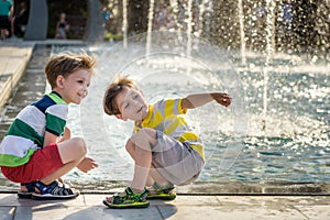 Cute toddler boy and older brothers, playing on a jet fountains with water splashing around, summertime