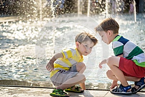 Cute toddler boy and older brothers, playing on a jet fountains with water splashing around, summertime