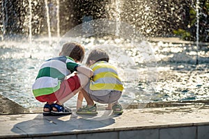 Cute toddler boy and older brothers, playing on a jet fountains with water splashing around, summertime