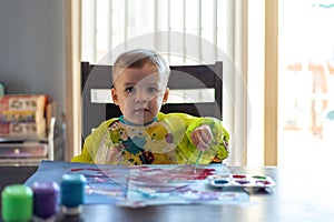 Cute toddler boy painting at the kitchen table