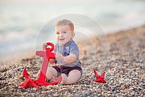 Cute toddler boy playing on the beach with sea red star and anchor