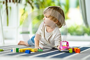 Cute toddler boy playing with blocks construction toy set on the floor at home. Daytime care creative activity. Kids having fun