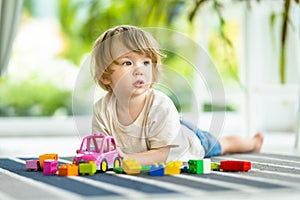 Cute toddler boy playing with blocks construction toy set on the floor at home. Daytime care creative activity. Kids having fun