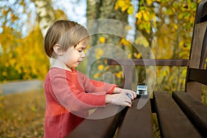 Cute toddler boy playing with red toy car outdoors. Kid exploring nature. Small child having fun with toys