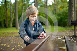 Cute toddler boy playing with red toy car outdoors. Kid exploring nature. Small child having fun with toys. Autumn activities for
