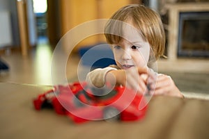 Cute toddler boy playing with red toy car. Small child having fun with toys. Kid spending time in a cozy living room at home