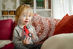 Cute toddler boy playing with red toy car. Small child having fun with toys. Kid spending time in a cozy living room at home