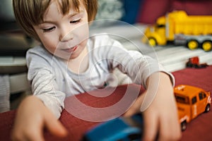 Cute toddler boy playing with toy cars. Small child having fun with toys. Kid spending time in a cozy living room at home