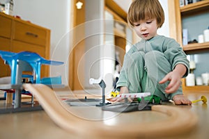 Cute toddler boy playing with wooden train set. Small child having fun with toys. Kid spending time in a cozy living room at home