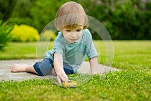 Cute toddler boy playing with yellow toy car outdoors. Kid exploring nature. Small child having fun with toys