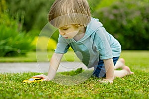 Cute toddler boy playing with yellow toy car outdoors. Kid exploring nature. Small child having fun with toys