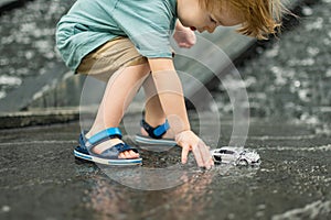 Cute toddler boy playing with yellow toy car outdoors. Kid having fun with water in city fountain. Summer activities for children