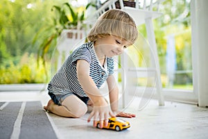 Cute toddler boy playing with yellow toy car. Small child having fun with toys. Kid spending time in a cozy living room at home