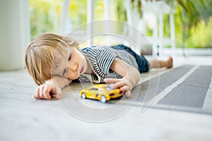 Cute toddler boy playing with yellow toy car. Small child having fun with toys. Kid spending time in a cozy living room at home