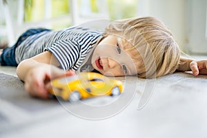 Cute toddler boy playing with yellow toy car. Small child having fun with toys. Kid spending time in a cozy living room at home