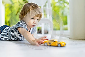 Cute toddler boy playing with yellow toy car. Small child having fun with toys. Kid spending time in a cozy living room at home