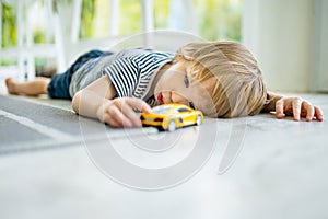 Cute toddler boy playing with yellow toy car. Small child having fun with toys. Kid spending time in a cozy living room at home