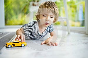 Cute toddler boy playing with yellow toy car. Small child having fun with toys. Kid spending time in a cozy living room at home