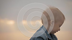 Cute toddler boy, sitting on the grass on sunset.