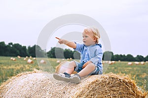 Cute toddler boy sitting on haystacks at wheat field.