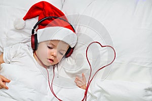 A cute toddler boy is sleeping in a santa hat and red headphones and near the wiring in the form of the heart