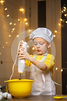 Cute toddler boy using hand blender to dough to cake . Preparing healthy meal in the kitchen