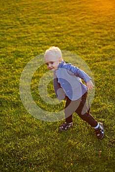 Cute toddler boy walking on green grass meadow sunset evening. Walking till sunset. Kid enjoy walk in park. Kindergarten