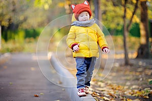 Cute toddler boy wearing hat with ears playing outdoors at autumn day