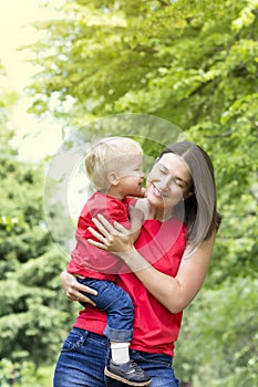 Cute toddler boy whispers in the mother`s ear. Kid kisses mom on the cheek. Very emotional mom and baby. Family look clothing. Co