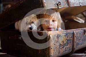 Cute toddler child, blond boy, hiding in a big suitcase in the attic, looking scared