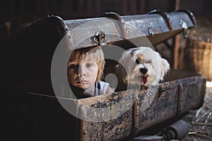 Cute toddler child, blond boy, hiding in a big suitcase in the attic, looking scared