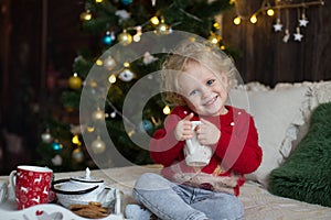 Cute toddler child, boy in a Christmas outfit, playing in a wooden cabin on Christmas, decoration around him. Child reading book